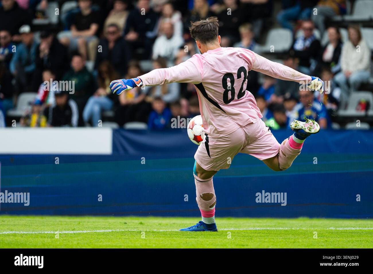 Torhüter in rosafarbenem Trikot tritt den Ball während eines Fußballspiels in einem überfüllten Stadion, dynamische Sportaktivitäten von hinten Stockfoto