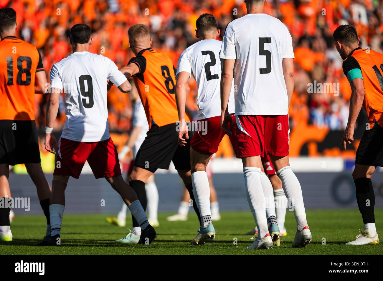 Professionelle Fußballspieler in weißen und orangefarbenen Uniformen stehen auf dem Spielfeld während eines intensiven Fußballstadions mit Fans. Stockfoto