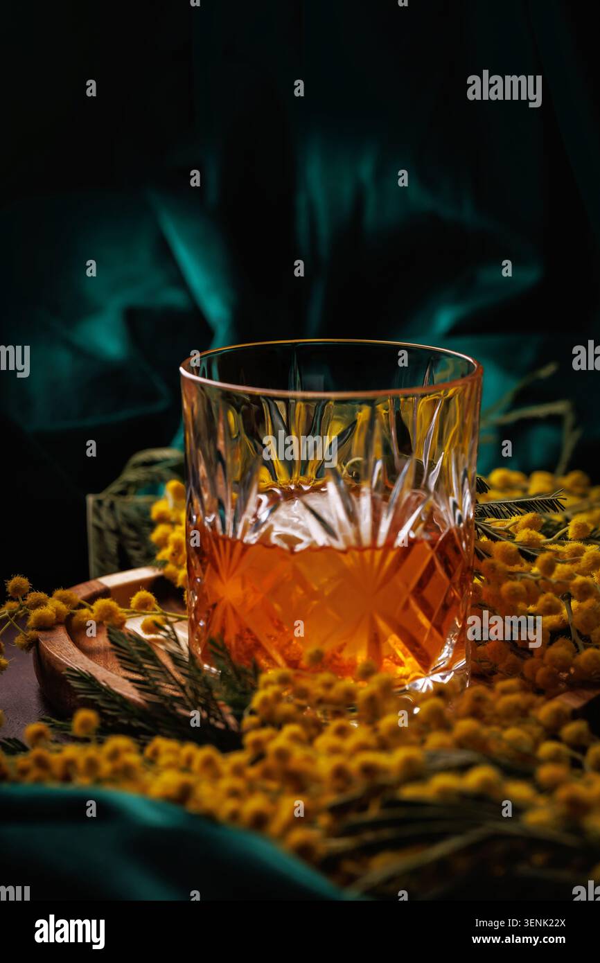 Whiskey mit Eis in Kristallglas mit Mimosa Flowers Spring Alcohol Konzept Stockfoto