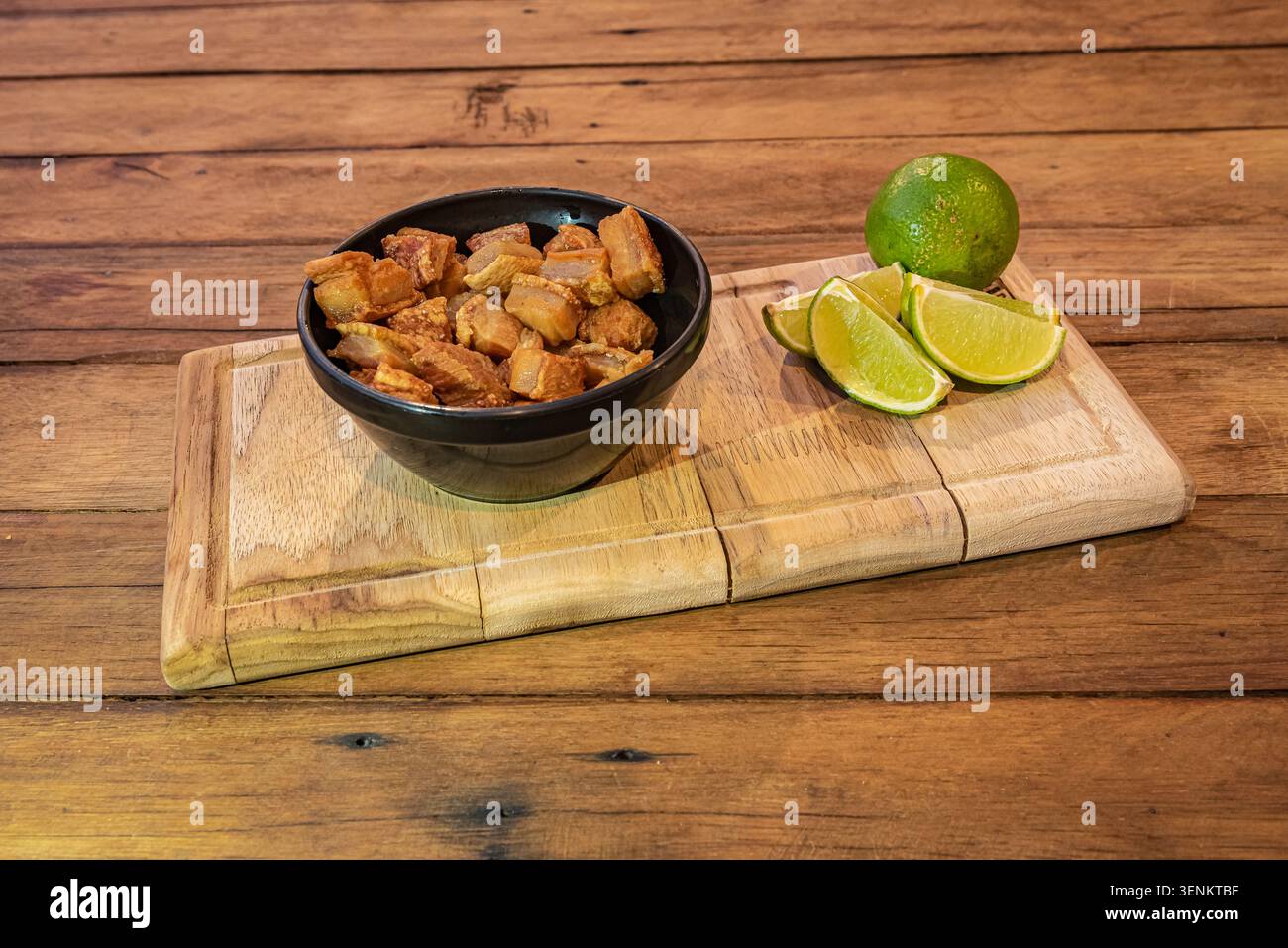 Nahaufnahme des Stilllebens mit brasilianischem Schweinebauchknacken, mit frischen Limettenkeilen auf rustikalem Holzbrett, mit warmem goldenem Licht. Perfekt für Stockfoto