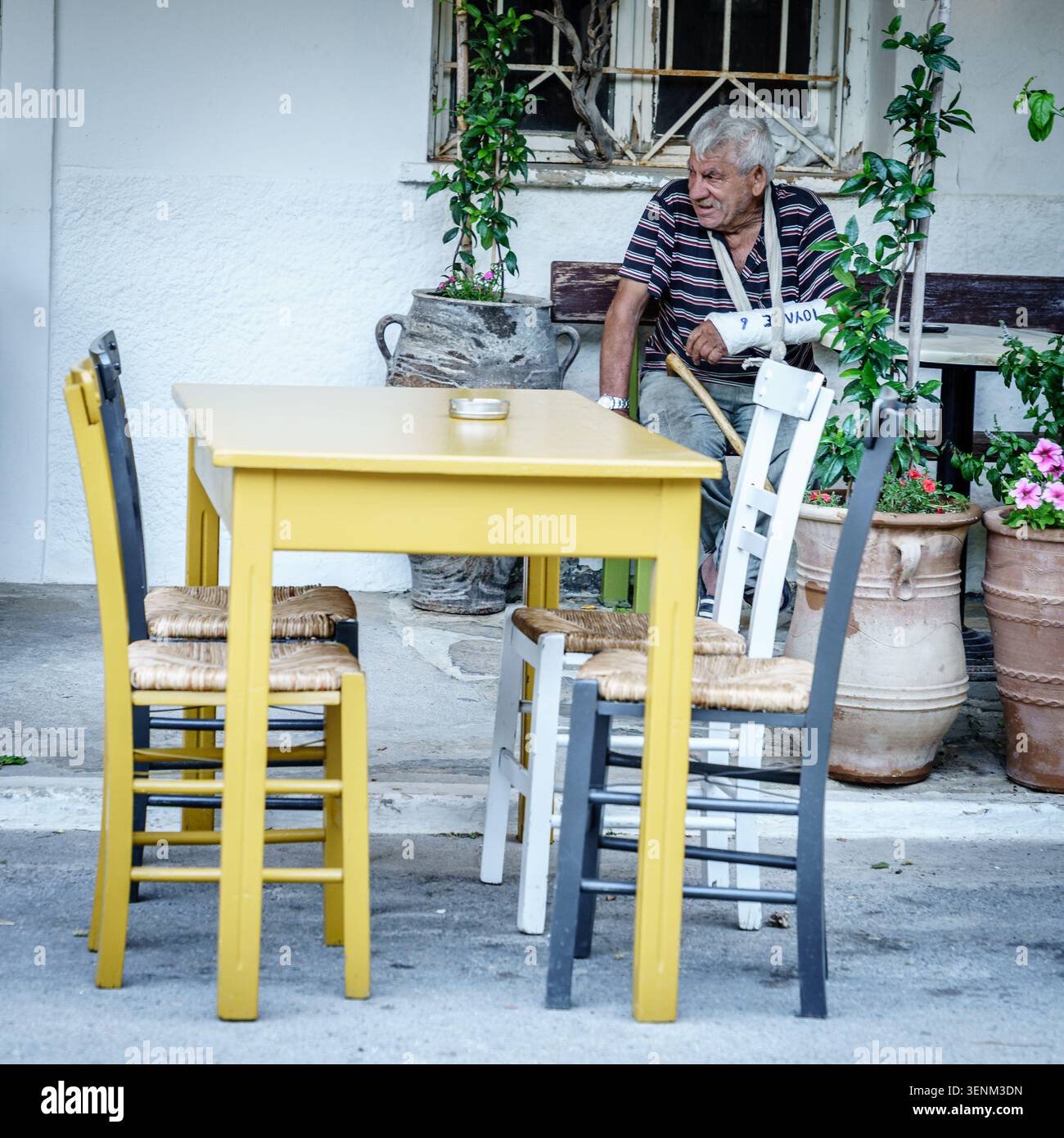 24. Juni 2022, Kreta, Griechenland: Ein einheimischer älterer Mann mit gegossenem Arm in einem Straßencafé im Dorf Kroustas, Kreta, Griechenland Stockfoto