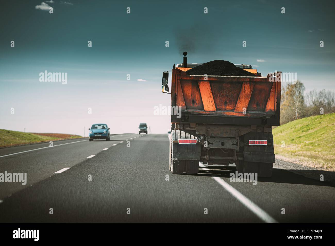 Ein orangener Kipplaster und ein White Box Truck fahren auf einer Autobahn. Stockfoto
