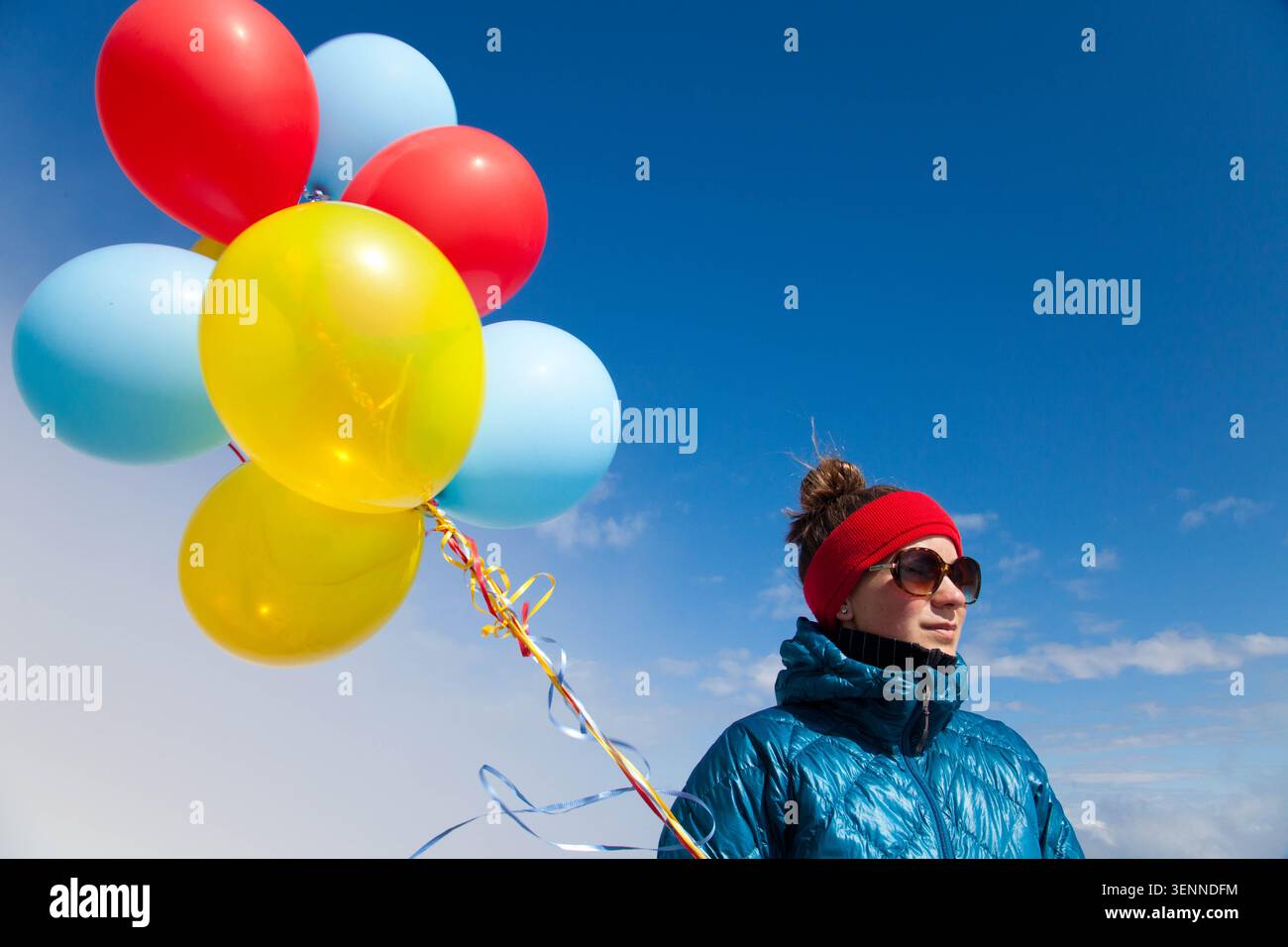 Frau in Winterkleidung hält bunte Ballons vor blauem Himmel Stockfoto