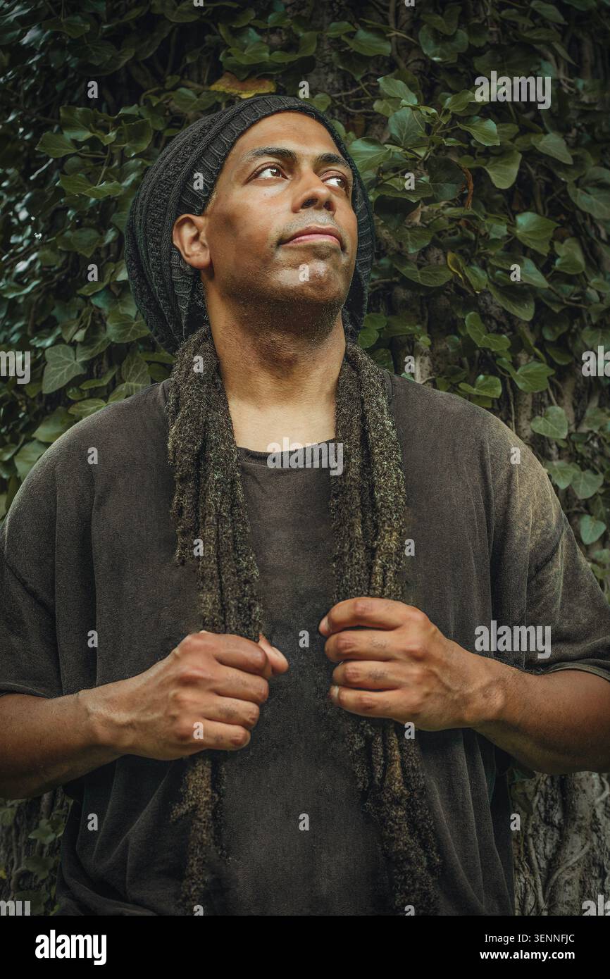 Ein nachdenklicher Mann mit Dreadlocks, der an der Efeuwand steht Stockfoto