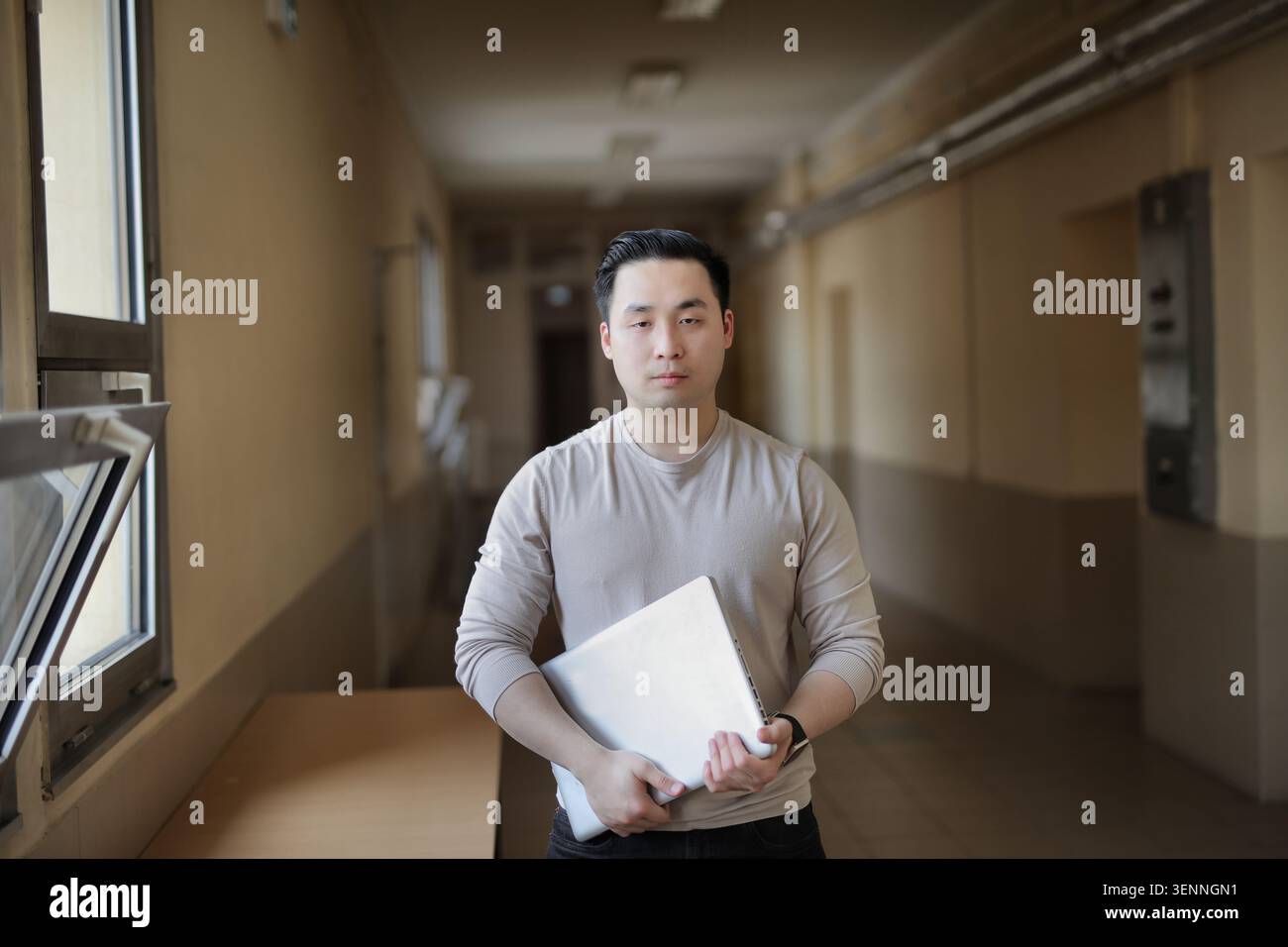 Junger asiatischer Student, der Laptop in leerem Flur hält Stockfoto