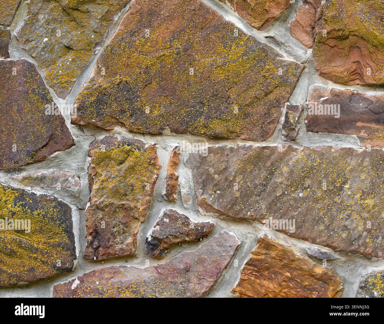Nahaufnahme der Felsenwand mit flachen, unebenen Steinen in verschiedenen Größen, Formen und Farben, dicken Rissmörtelfugen und Moos, die die Steine bedecken Stockfoto