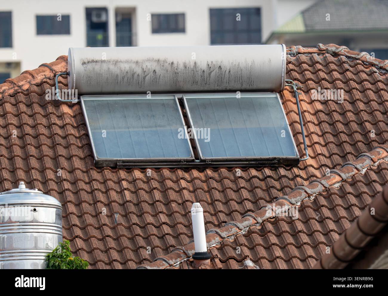 Dachblick auf eine Solaranlage mit Kollektorpaneelen und Speichertank, die auf einem verwitterten Dach aus braunem Lehm installiert sind. Stockfoto