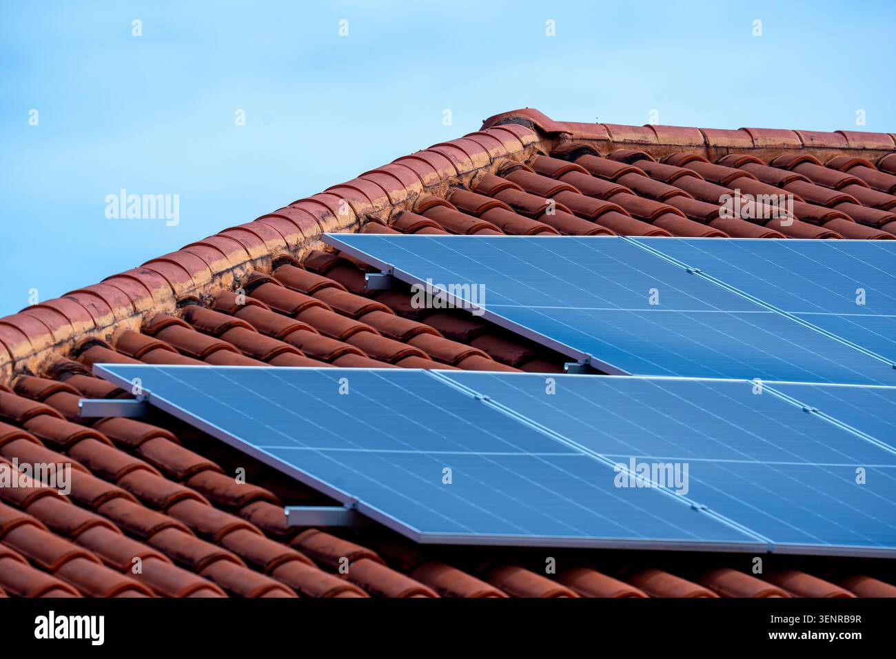 Detaillierte architektonische Aufnahme von zeitgenössischen Photovoltaik-Solarmodulen, die auf einem Wohndach aus orangen Terrakotta-Tonziegeln installiert sind. Stockfoto