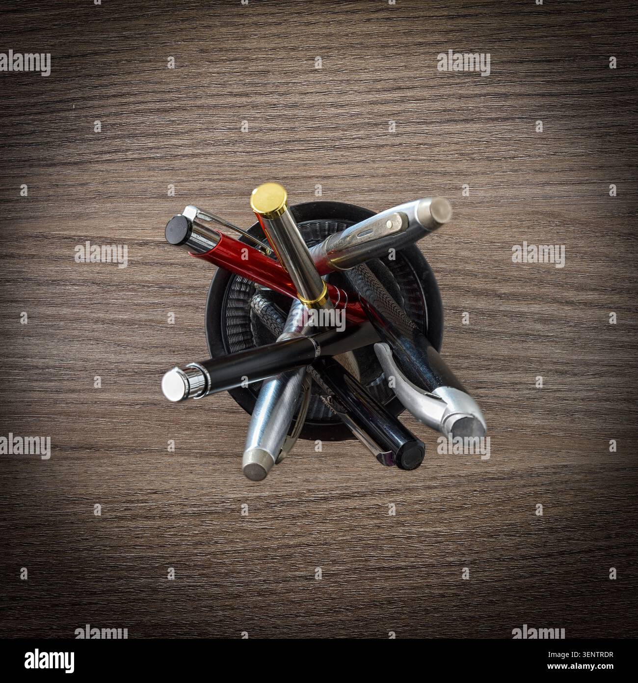 Ansicht von oben auf verschiedene Stifte und Schreibgeräte, die in einem Halter auf einer hölzernen Schreibtischoberfläche angeordnet sind. Stockfoto