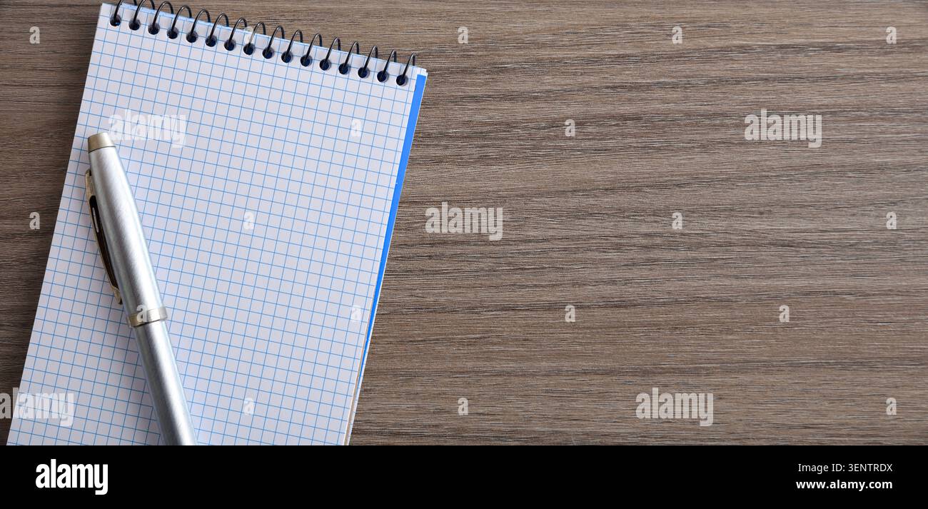 Minimalistischer Draufsicht eines leeren Spiralnotizbuches und Silberstifts auf einem Holztisch, der Platz zum Kopieren von Notizen, Planungen oder kreativen Schreiben bietet. Stockfoto