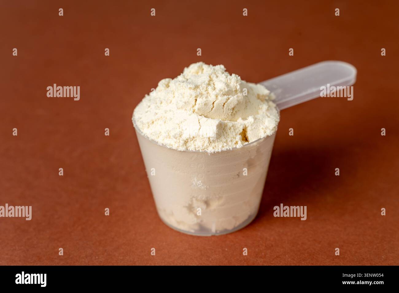 Messlöffel mit Proteinpulver auf braunem Hintergrund, Sporternährung und Nahrungsergänzungsmittel Stockfoto