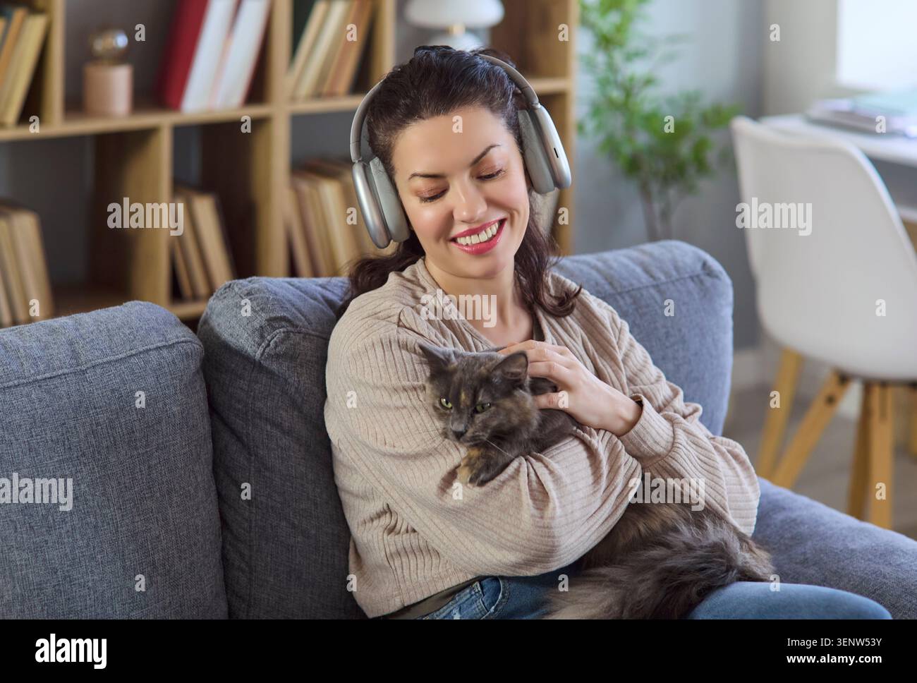 Lächelnde Frau in Kopfhörern kuschelt Katze auf Sofa zu Hause, hört Musik Stockfoto