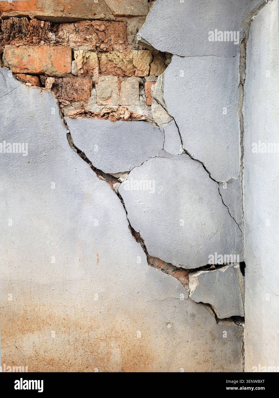 Risse und ein Loch in der verputzten Oberfläche der Mauer eines alten Ziegelgebäudes. Riesiger großer Riss zwischen den Wänden aufgrund der Feuchtigkeit. Stockfoto