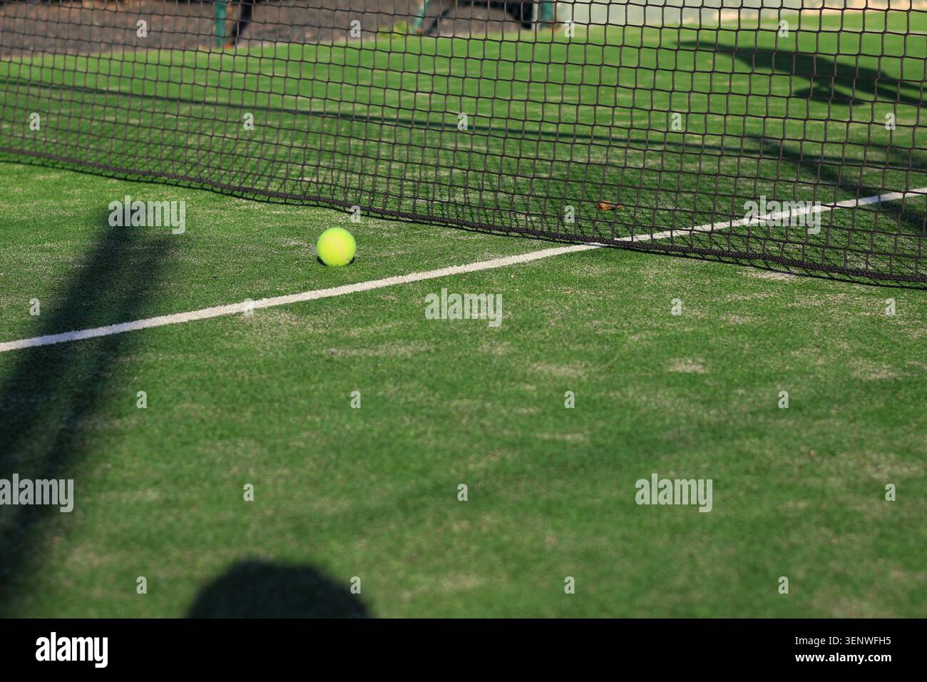 Blick auf grünen Kunstrasen mit einem gelben Tennisball und einem schwarzen Netz Stockfoto