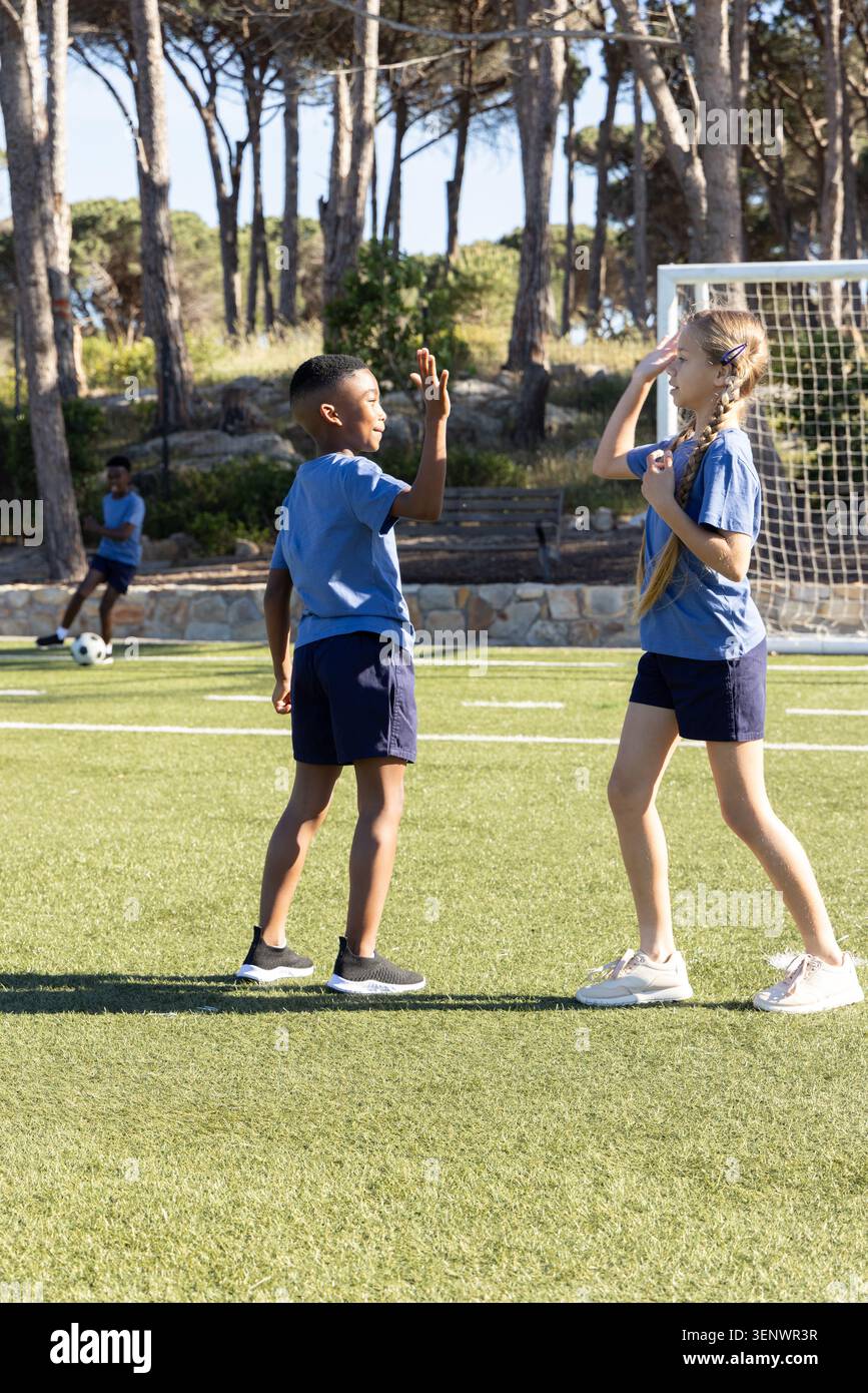Verschiedene Schulkinder, Jungen und Mädchen in blauen Trikots, tauschen High-Fives auf dem Fußballfeld in der Nähe des Tores aus Stockfoto