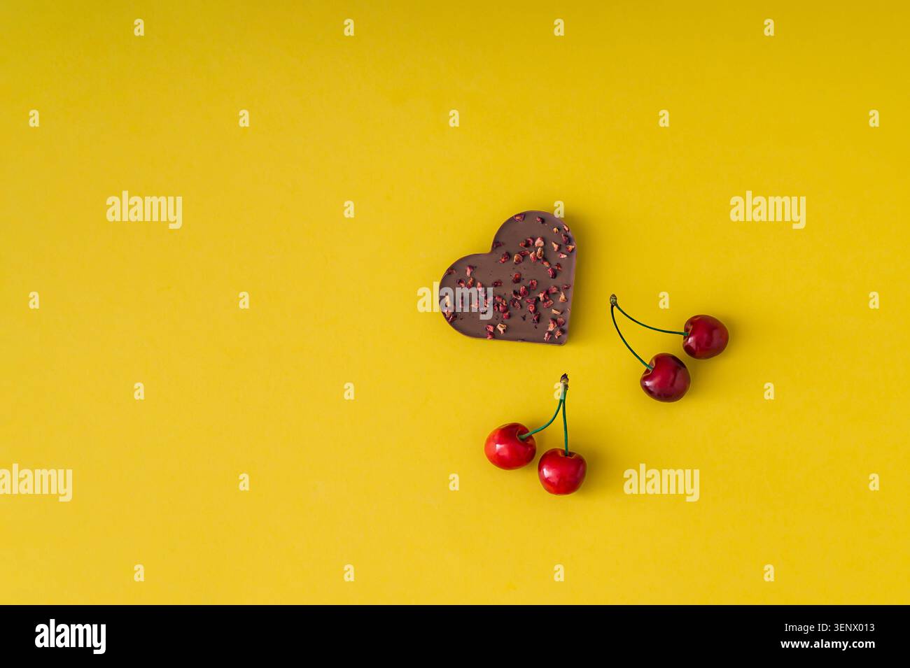 Herzförmige Schokolade und frische rote Kirschen auf gelbem Hintergrund mit Kopierraum. Romantisches Essenskonzept. Flache Lagen. Banner mit Draufsicht. Stockfoto
