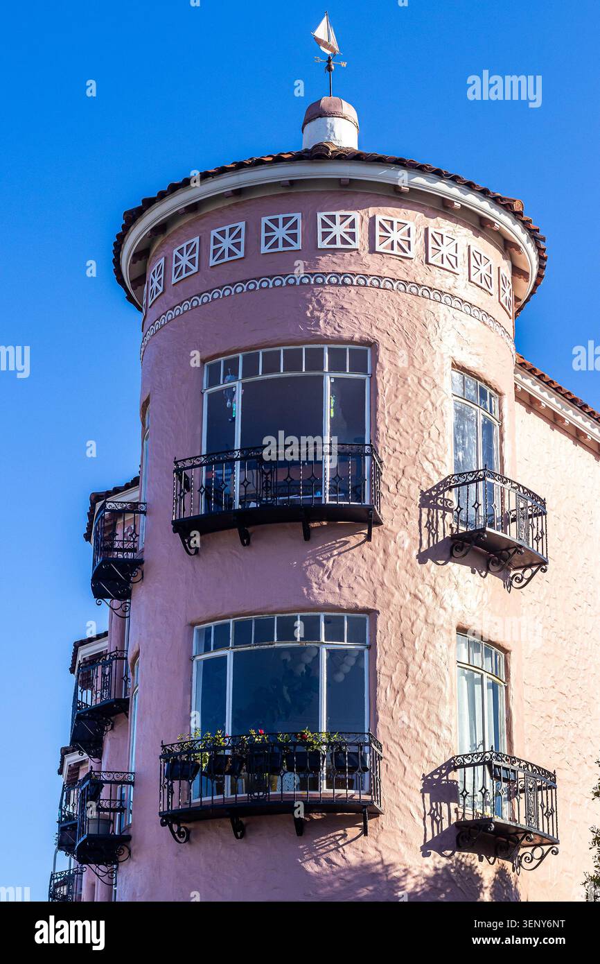 Pinkfarbenes Art déco-Apartmentgebäude mit Turm, Erkerfenstern, Balkonen und rotem Fliesendach vor einem klaren blauen Himmel in San Francisco, Kalifornien Stockfoto