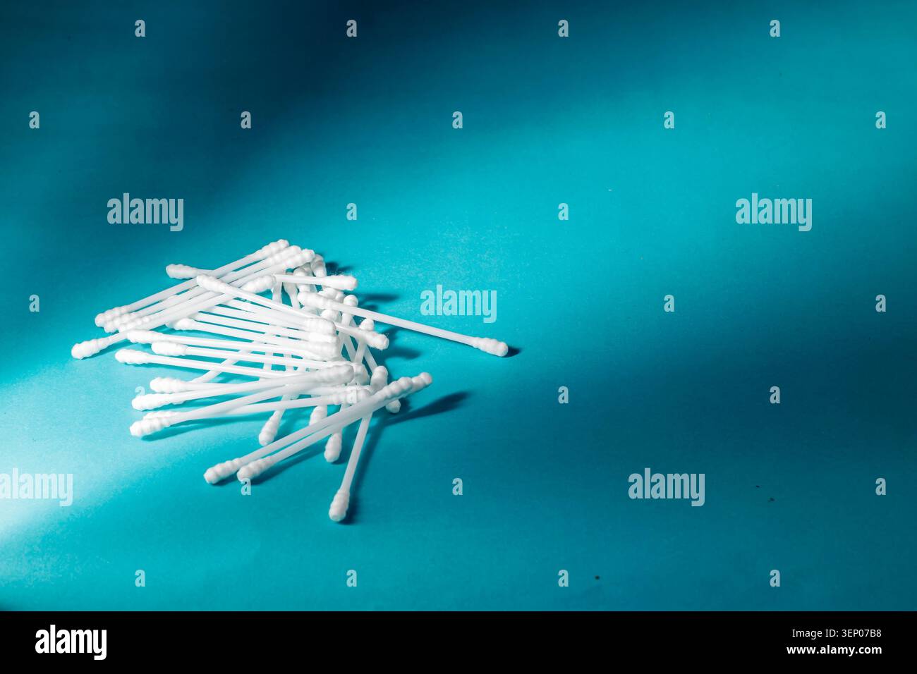 Ein verstreuter Haufen weißer Baumwollknospen oder Q-Tips aus Kunststoff, die für Körperhygiene, Kosmetik und Ohrreinigung vor hellcyanfarbenem Hintergrund verwendet werden. Hochwertige Fotos Stockfoto