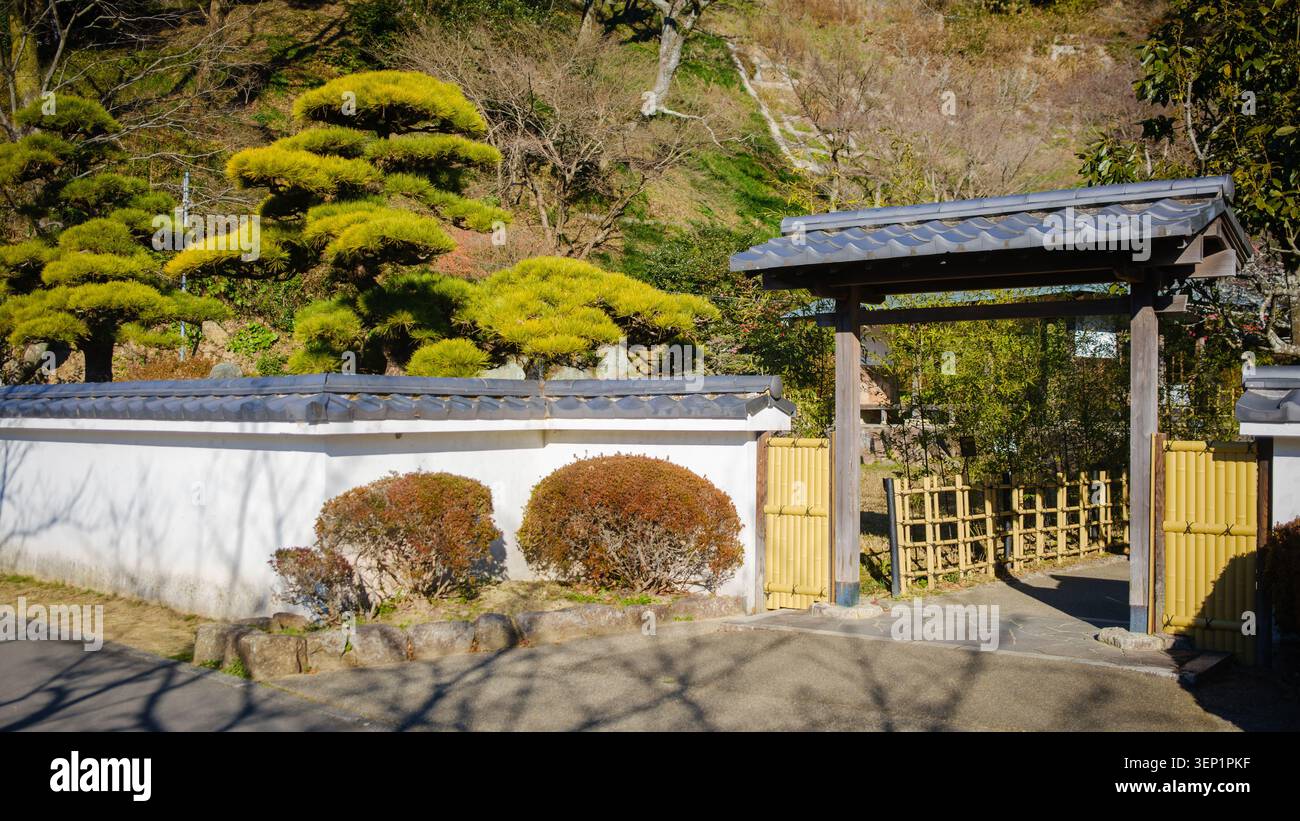 Ein einfaches Holztor mit Ziegeldach, das in eine traditionelle weiße Putzwand im japanischen Garten im Rengeji-ike Park in Fujieda, Präfektur Shizuoka, eingebaut ist. Stockfoto