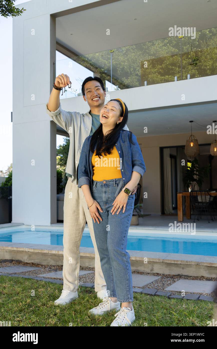 Diverse Paare stehen auf dem Rasen am Pool, Mann hält Schlüsselanhänger, während die Frau lacht Stockfoto