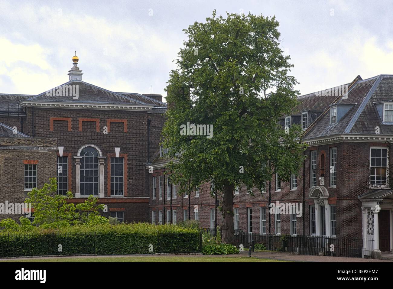 Die historische Backsteinfassade des Kensington Palace, London, mit einem zentralen Innenhof, einem großen Baum und einem goldenen Finial auf dem Dach. Stockfoto