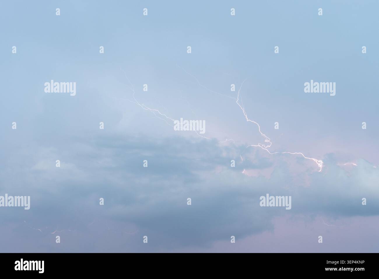 Ein beeindruckendes Bild, das einen starken Blitz aufnimmt, der die dunklen, stürmischen Wolken vor einem blassblauen und violetten Abendhimmel beleuchtet und das R zeigt Stockfoto