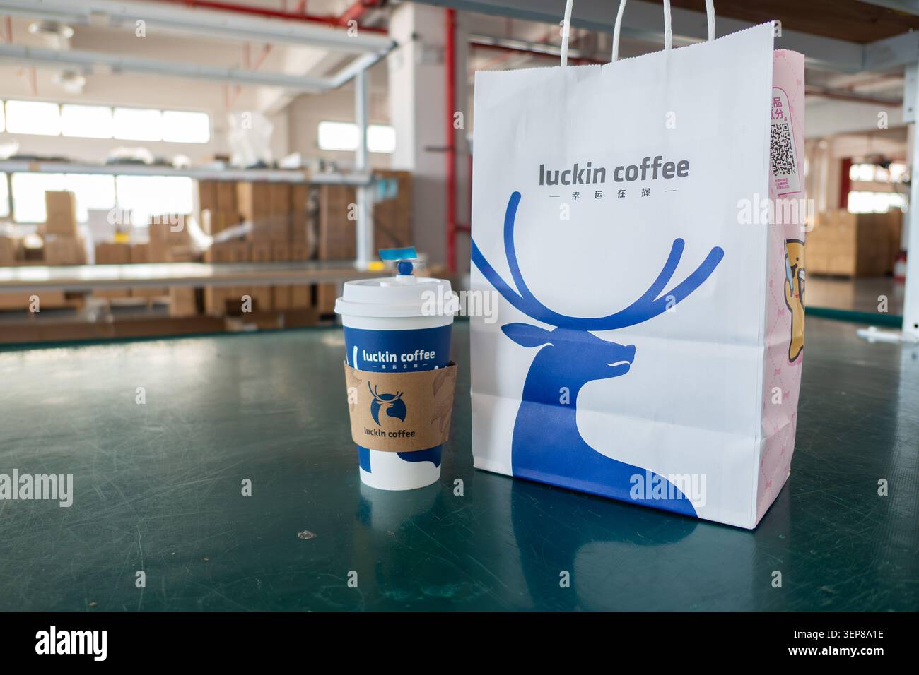 ZHONGSHAN China-14. Februar 2026: Luckin Kaffee Einweg-Papier-Kaffeetasse mit Kraftwärmehülle neben gebrandetem weißem Hirschdruckpapier Takea platziert Stockfoto