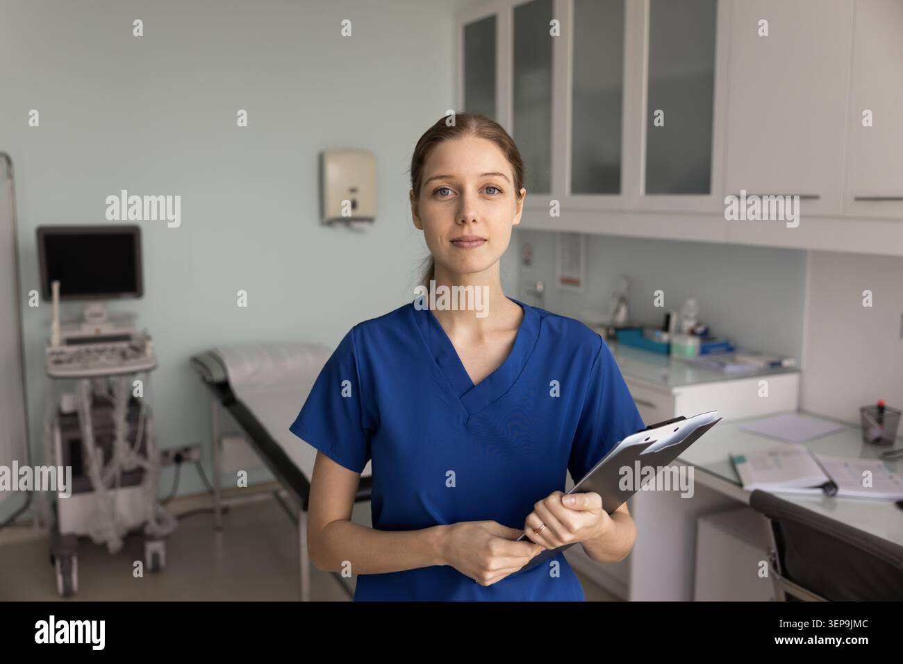 Schwester in blauen Schutten hält Klemmbrettständer im Untersuchungsraum Stockfoto