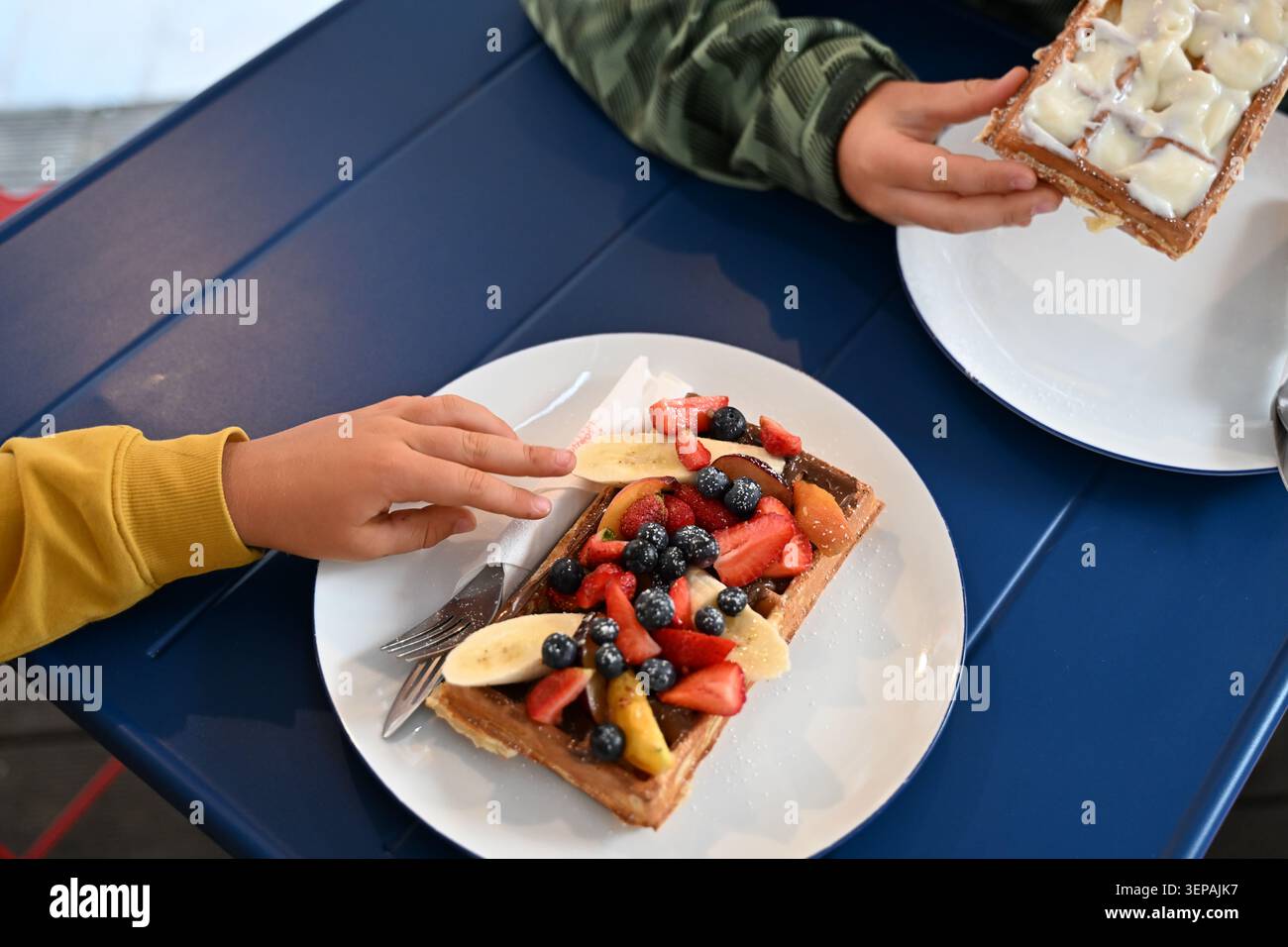 Waffeln mit frischem Obst und Schlagsahne mit Kindern, die nach Essen greifen Stockfoto