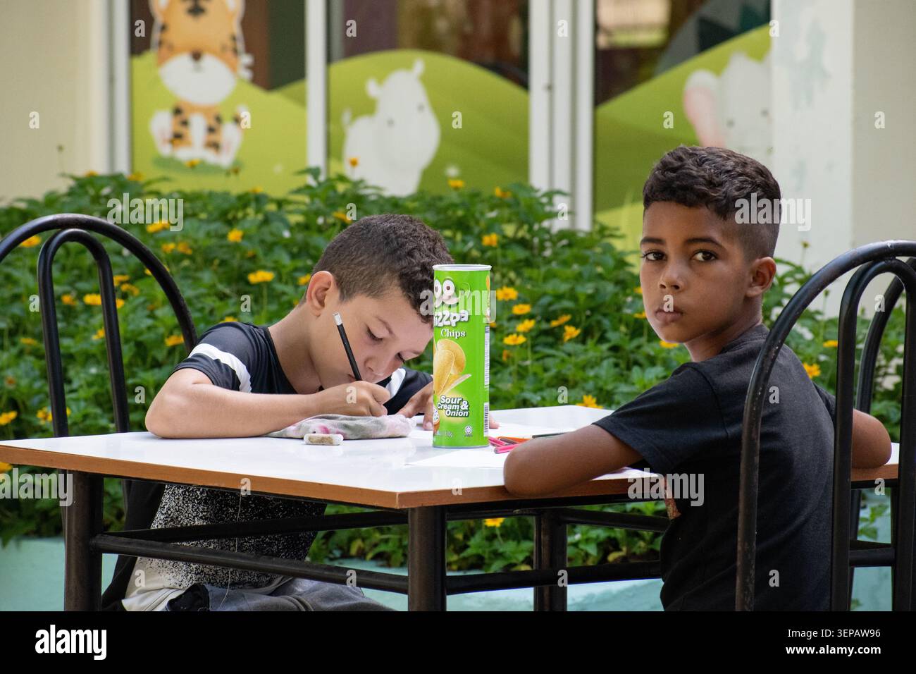 Zwei Jungen, die an einem Tisch im Freien sitzen und während einer Gemeinschaftsaktion in Ciego de Ávila in die Kamera schauen Stockfoto