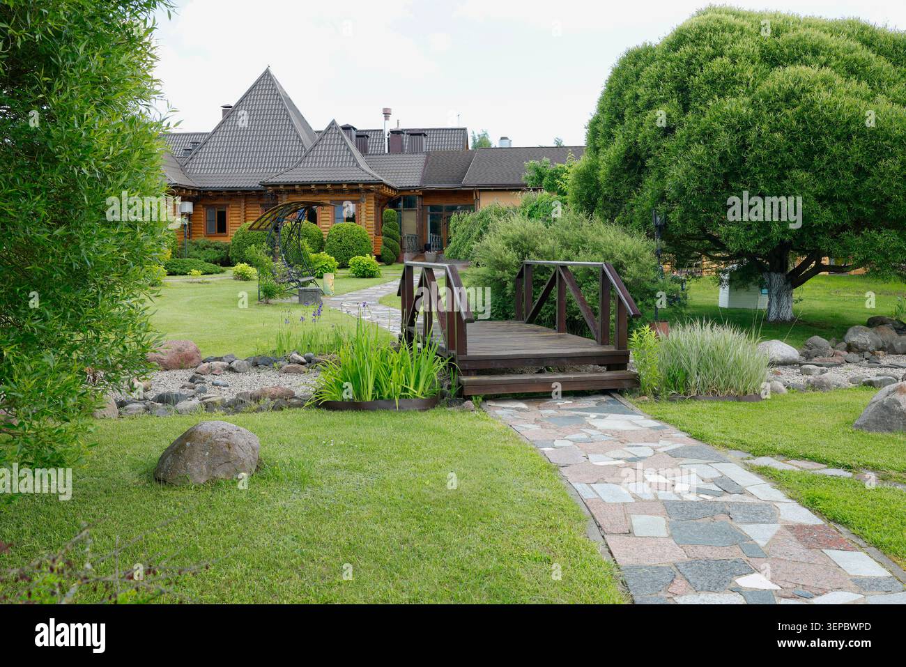 Professionelles Landschaftsprojekt mit gepflastertem Steingang, der zu einer kleinen Holzbrücke führt. Wunderschön gepflegter Garten im Hinterhof mit großem Stockfoto
