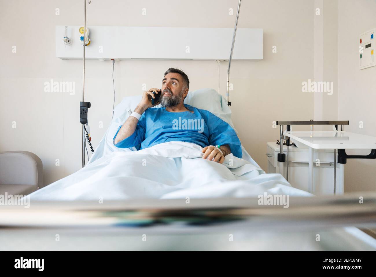 Reifer Mann empfängt Telefonanruf im Krankenhausbett Stockfoto
