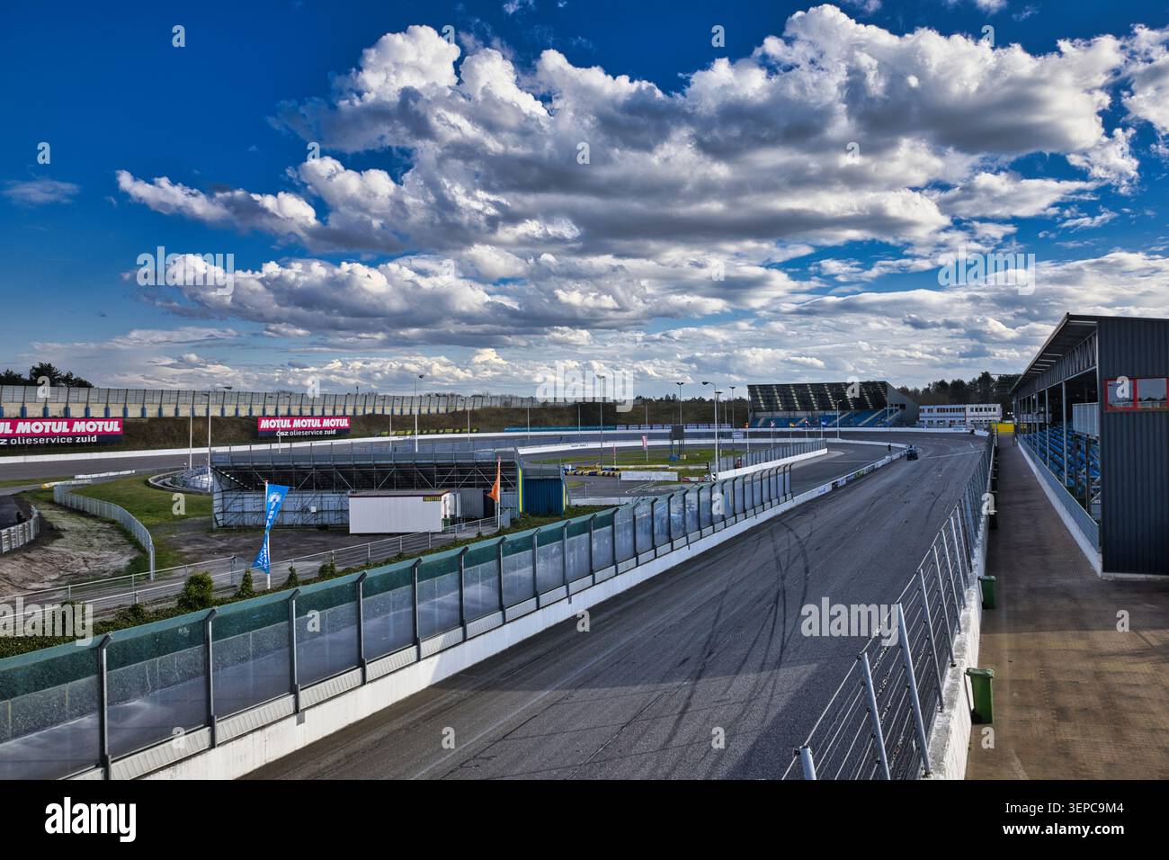 Leere Asphaltrennstrecke am Raceway Venray in der niederländischen Provinz Limburg unter einem dramatischen blauen Himmel mit großen Wolken. Stockfoto