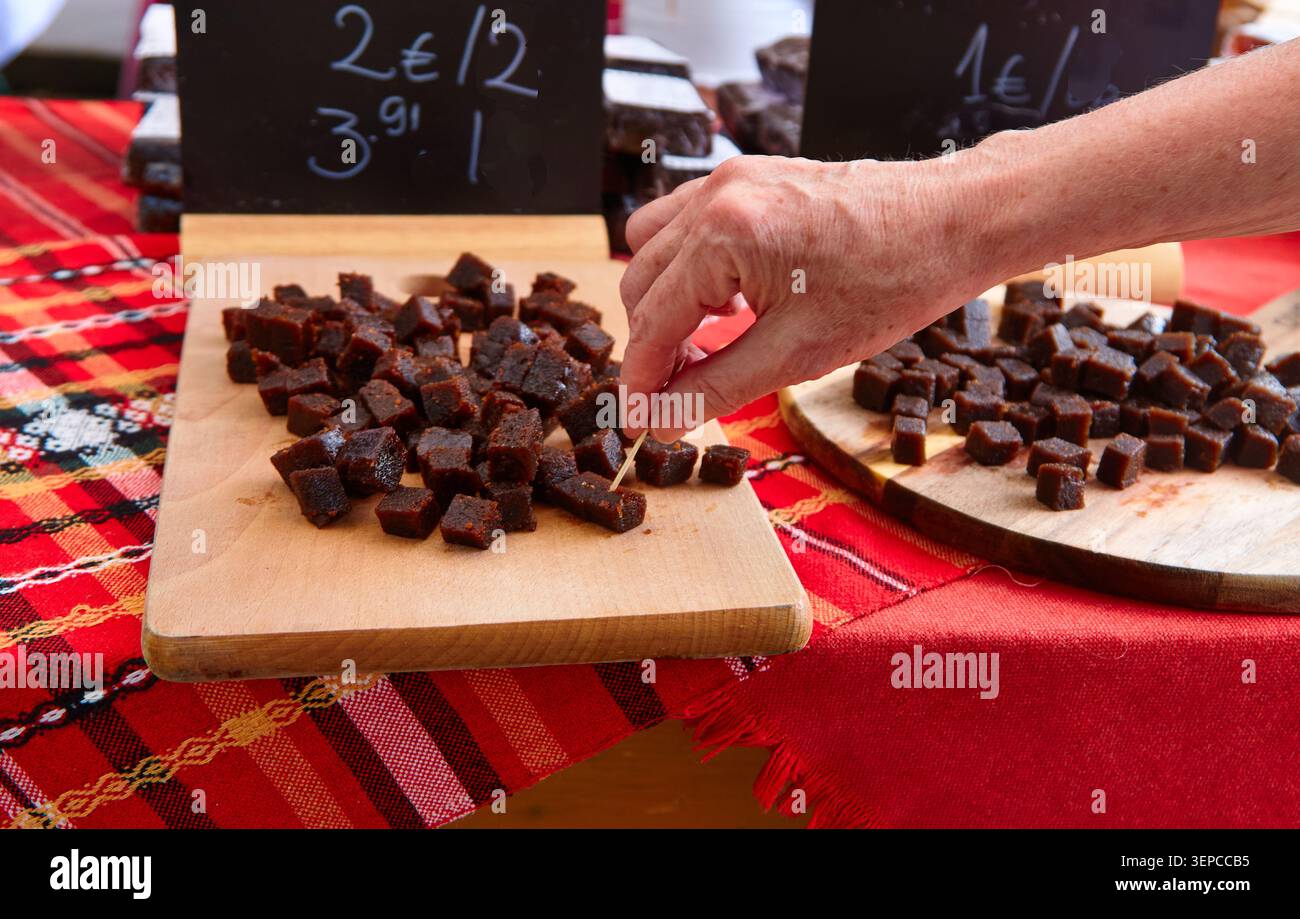 Bulgarische Fruchtmarmeladenwürfel sind auf Holzbrettern an einem Straßenstand angeordnet, mit einer Hand, die nach einem Stück greift, und farbenfrohen Preisschildern auf der Rückseite Stockfoto