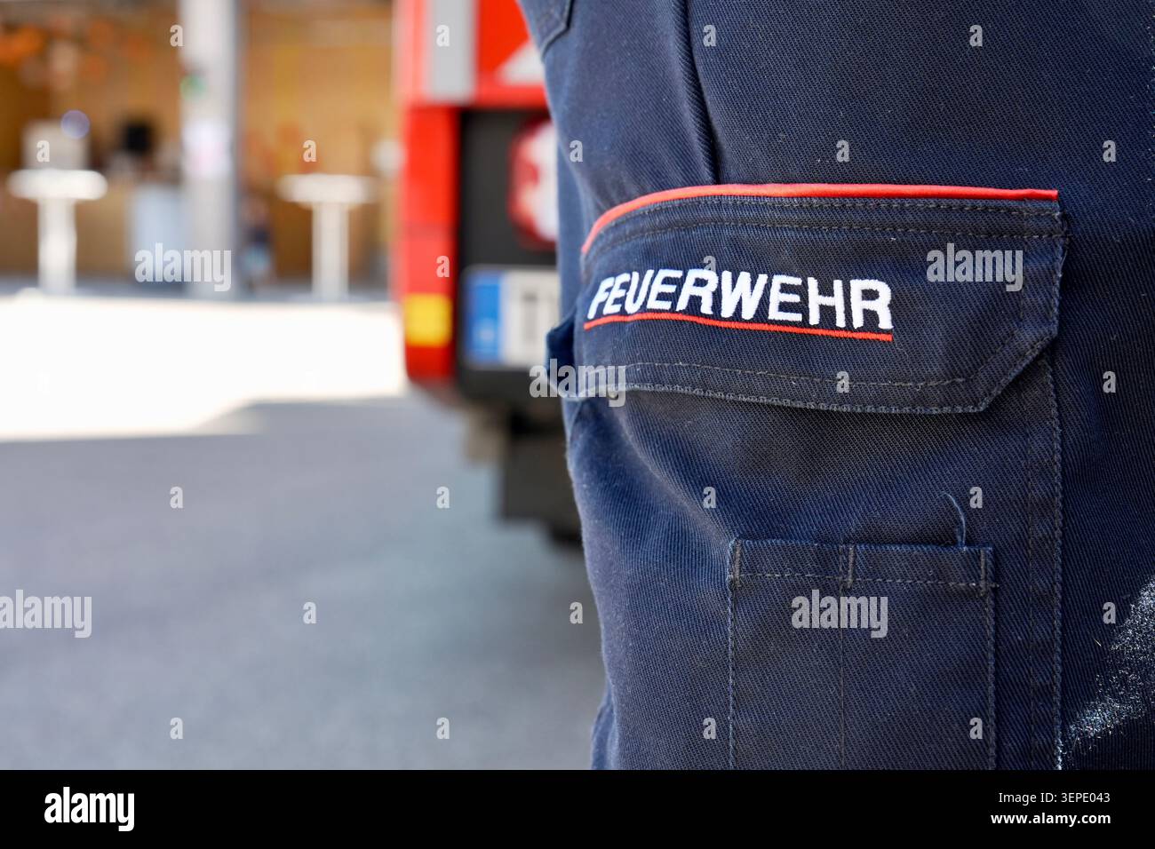 Nahaufnahme eines aufgestickten Feuerwehrflecks auf einer deutschen Feuerwehrwehruniform-Hülle, mit einem roten Feuerwehrauto im Hintergrund Stockfoto