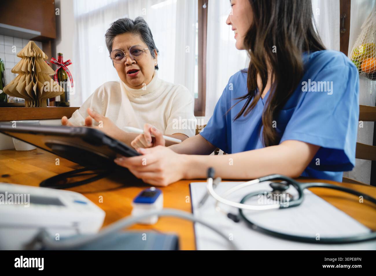 Asiatische Großmutter diskutiert Gesundheitsplan Facharzt häusliche Umgebung, professionelle Pflegeperson Notizen Tablette, ältere sprechen ernst und aus Stockfoto