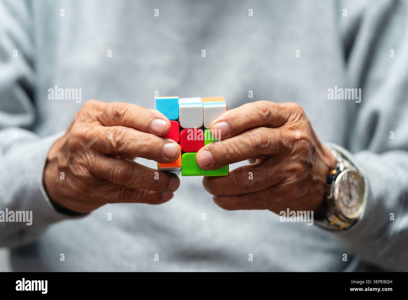 Nahaufnahme von älteren Händen, die einen teilweise gelösten bunten Würfel halten. Älterer Mann, der bunte Würfel spielt alzheimer-Vorbeugungstherapie, trainiert Gedächtniskogn Stockfoto