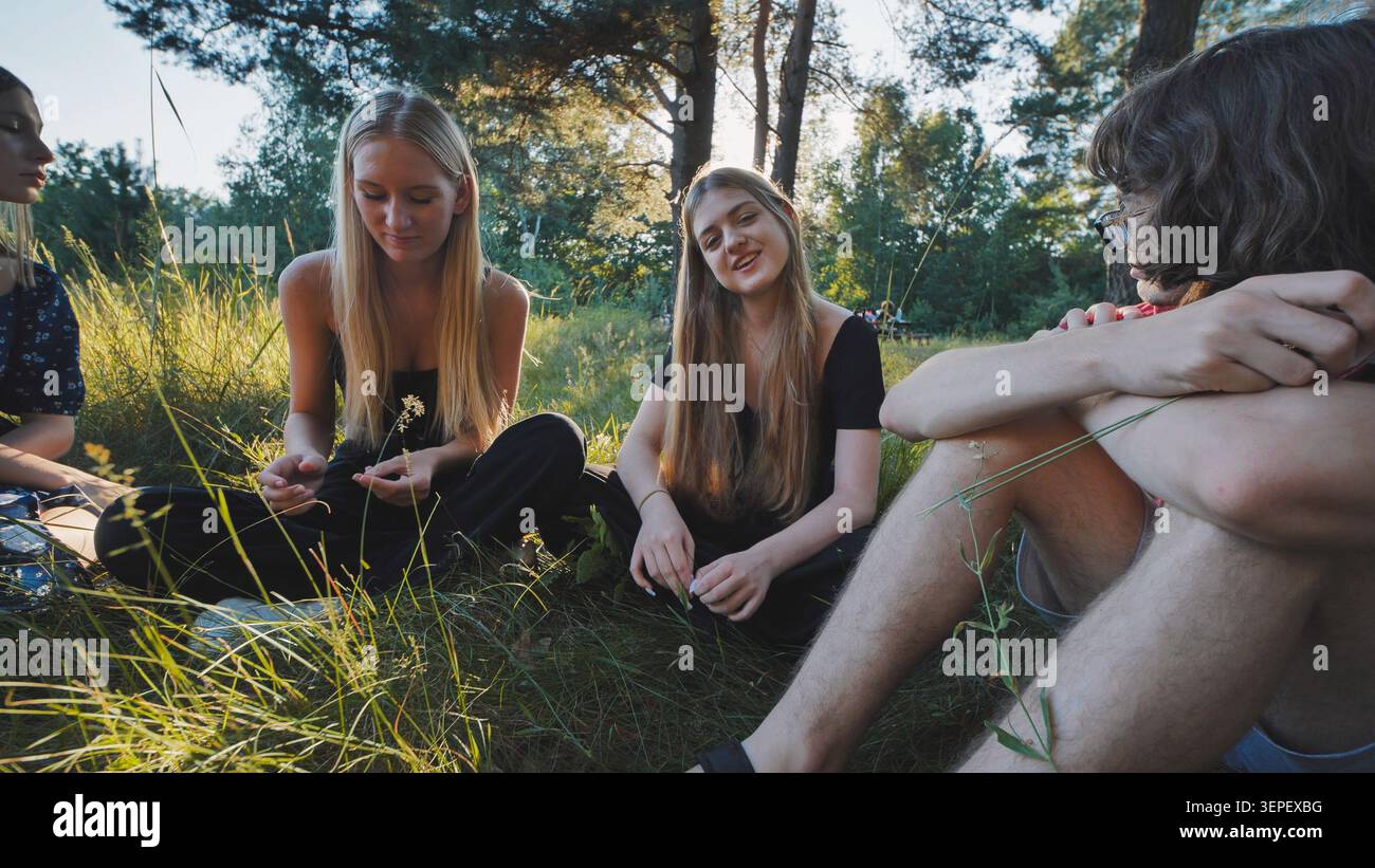 Freunde im Teenageralter entspannen sich auf grasbewachsenem Boden, verbinden sich und lachen während der Freizeit im Freien Stockfoto