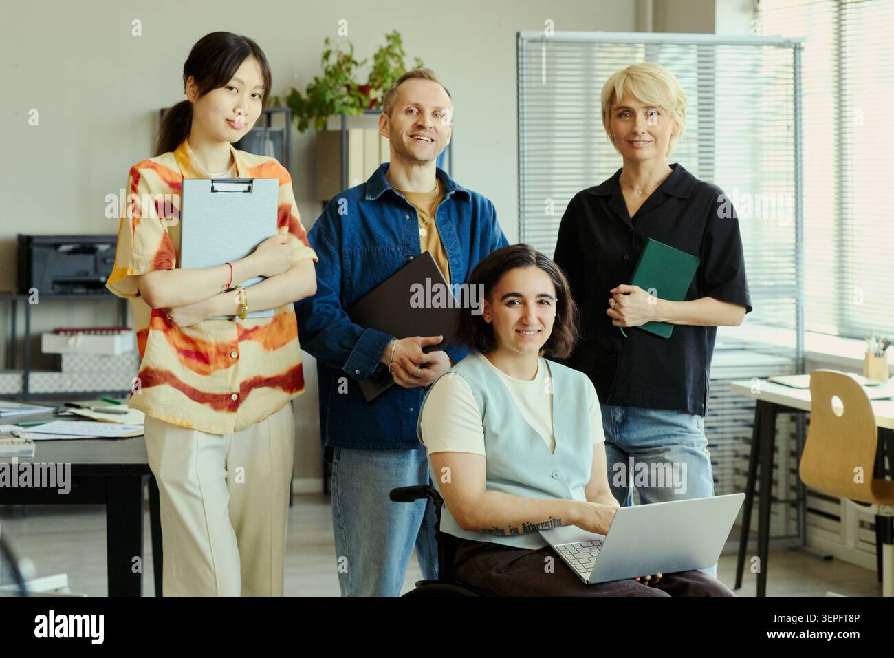 Porträt verschiedener junger erwachsener Kollegen, die mit Laptop und Dokumenten im Büro posieren und Teamarbeit und Integration repräsentieren. Ideal für Arbeitsplatzkultur, Personalwesen und Recruiting-Kampagnen Stockfoto