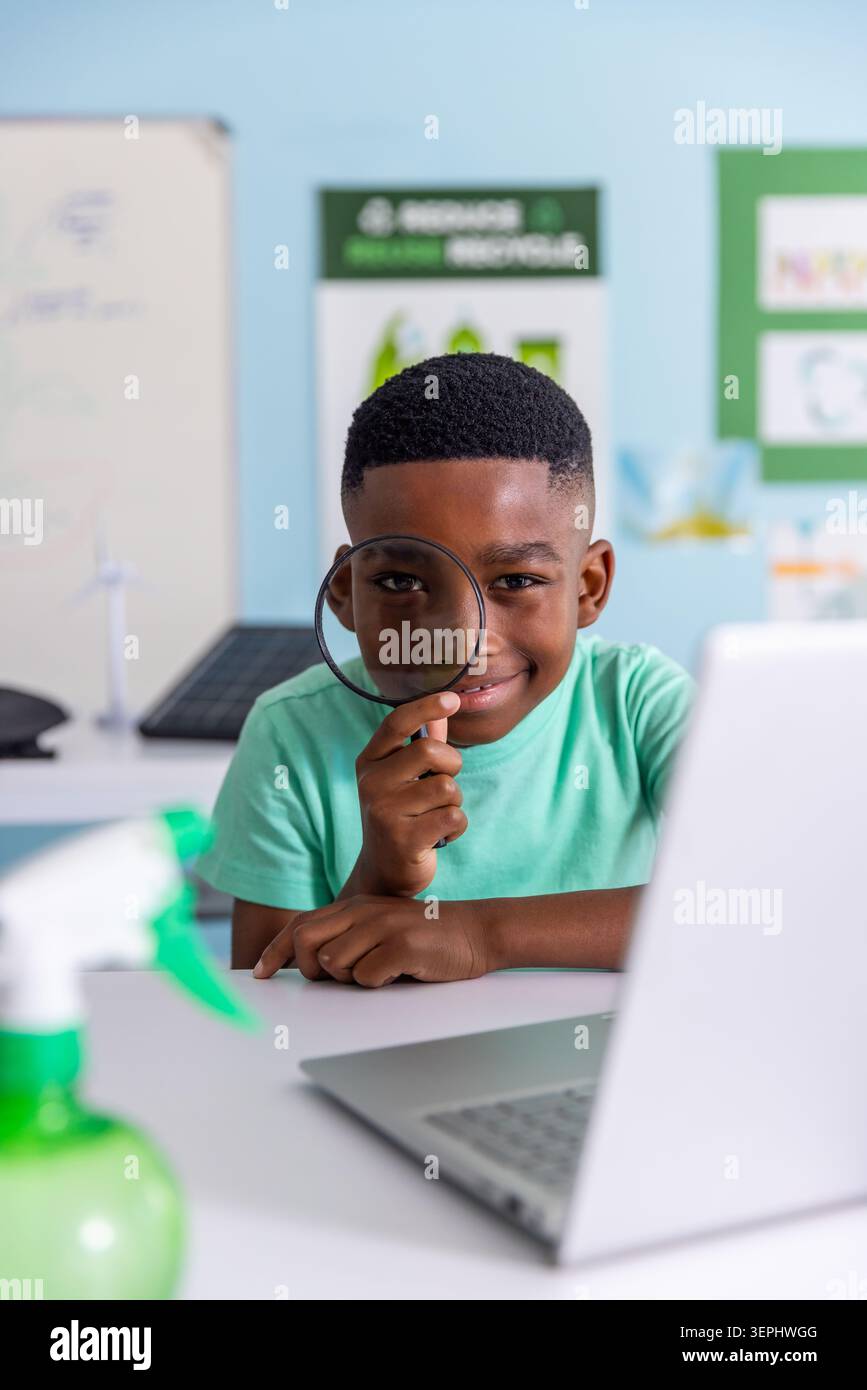 Afroamerikanischer Schuljunge mit Lupe, der in der Schule auf Laptop-Wind- und Solarmodelle blickt Stockfoto