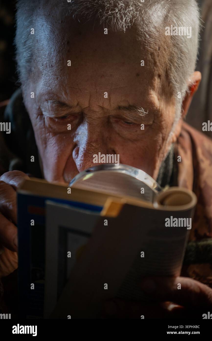 Ein älterer Mann liest den Text in einem Buch mit einer Lupe Stockfoto