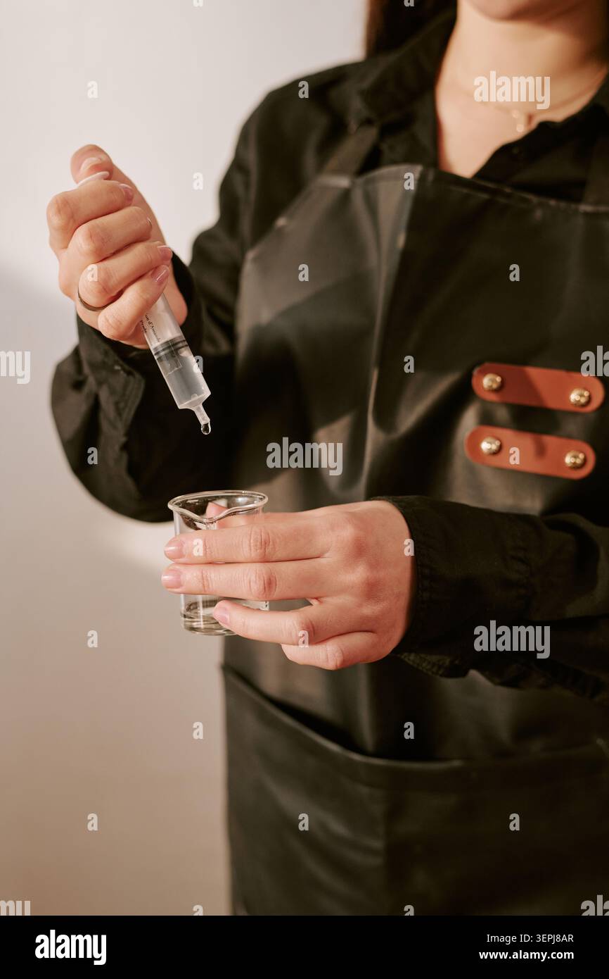 Erwachsene Frau, die Flüssigkeit im Becher für die Prüfung von Schönheitsprodukten misst Stockfoto