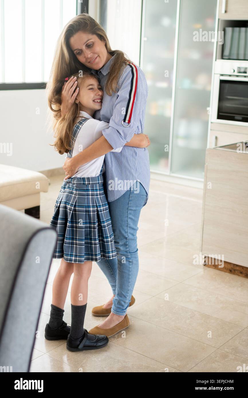 Liebevolle Mutter und Tochter im schulpflichtigen Alter, die sich vor dem Schultag zu Hause umarmen. Stockfoto