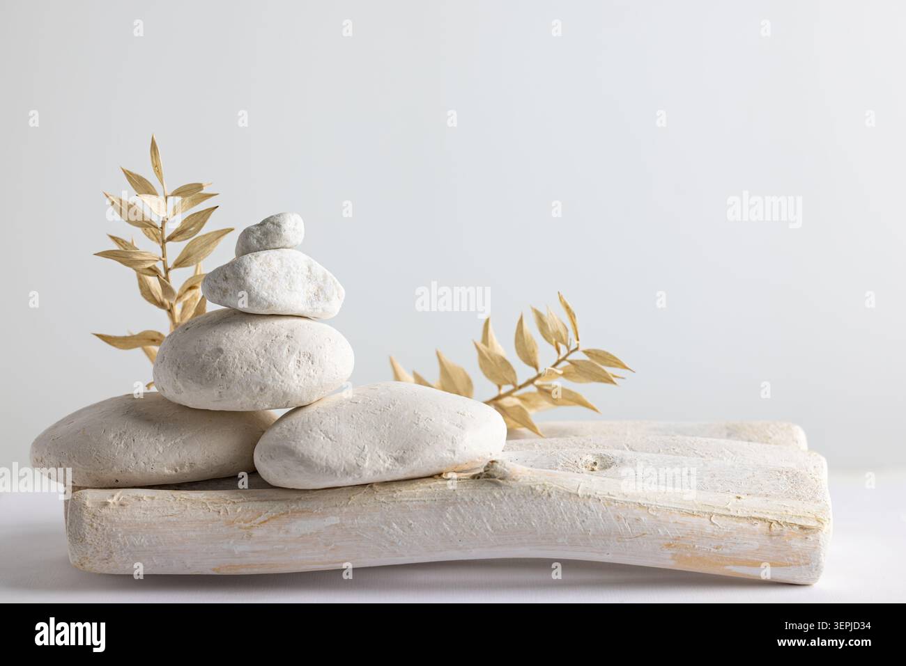 Weiße Kieselsteine auf rustikalem Holztablett mit getrockneten Blättern sorgen für Wellness-Balance und minimalistische Einrichtung Stockfoto