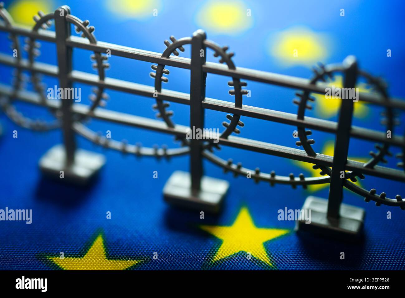 Miniaturzaun mit Stacheldraht auf EU-Flagge, symbolisches Bild der europäischen Asylreform Stockfoto