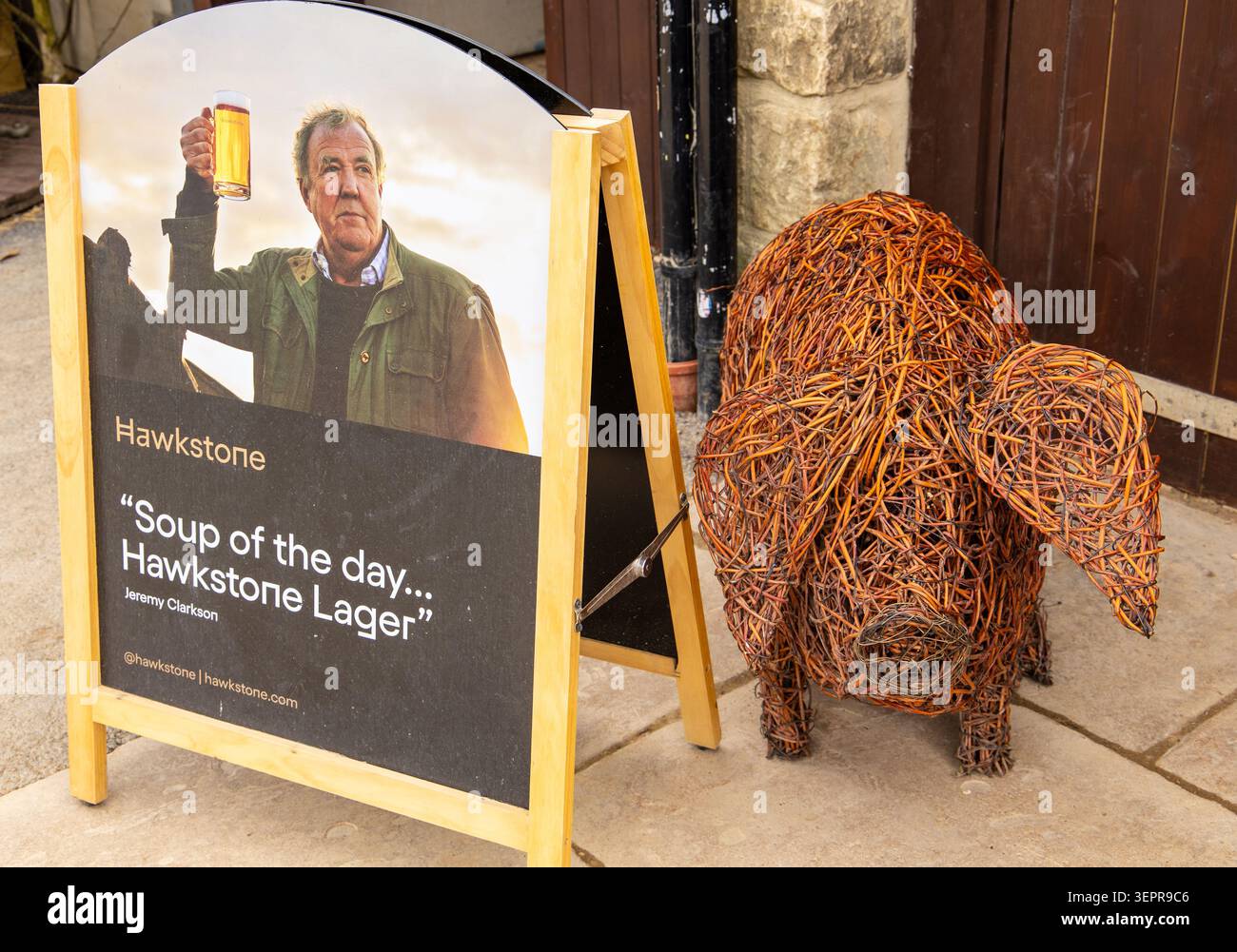 Ein hölzernes A-Rahmen-Schild, das das Lager von Hawkstone mit einem Foto von Jeremy Clarkson neben einer dekorativen, gewebten Korbskulptur eines Schweins markiert Stockfoto