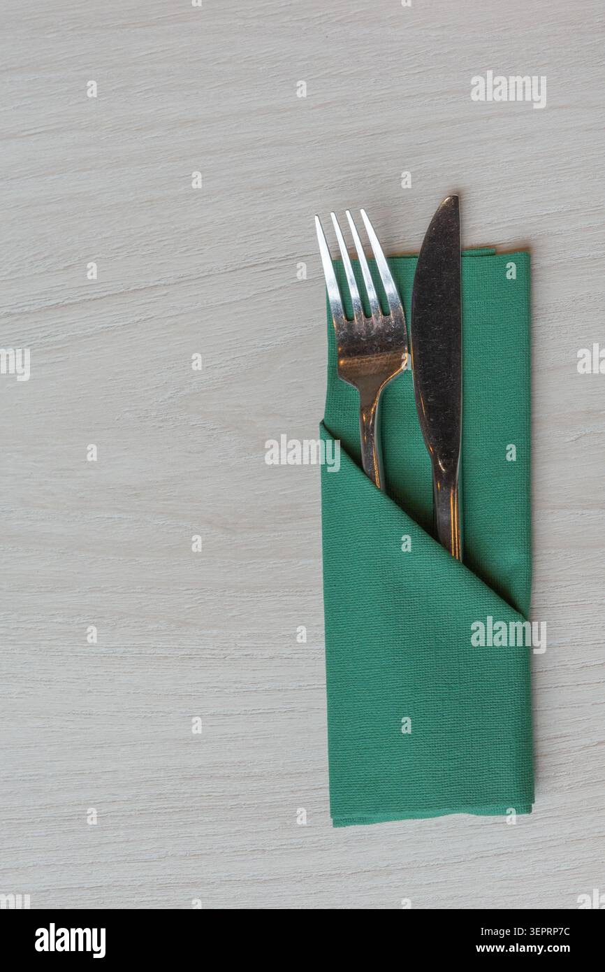 Gabel und Messer sind ordentlich in einer grünen Serviette auf einem hellen Holztisch angeordnet. Diese Einrichtung ist typisch für kulinarische Anlässe in einem Restaurant oder Café. Stockfoto