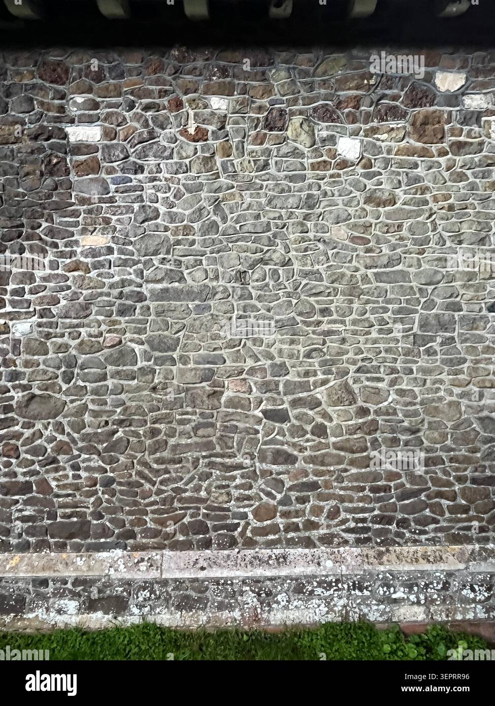 Verwitterte Steinmauer mit unregelmäßig geformten Steinen und natürlicher Oberflächenstruktur, die Farbvariationen und Details im Außenbereich zeigt. - Smartphone-aufgenommenes Stockfoto