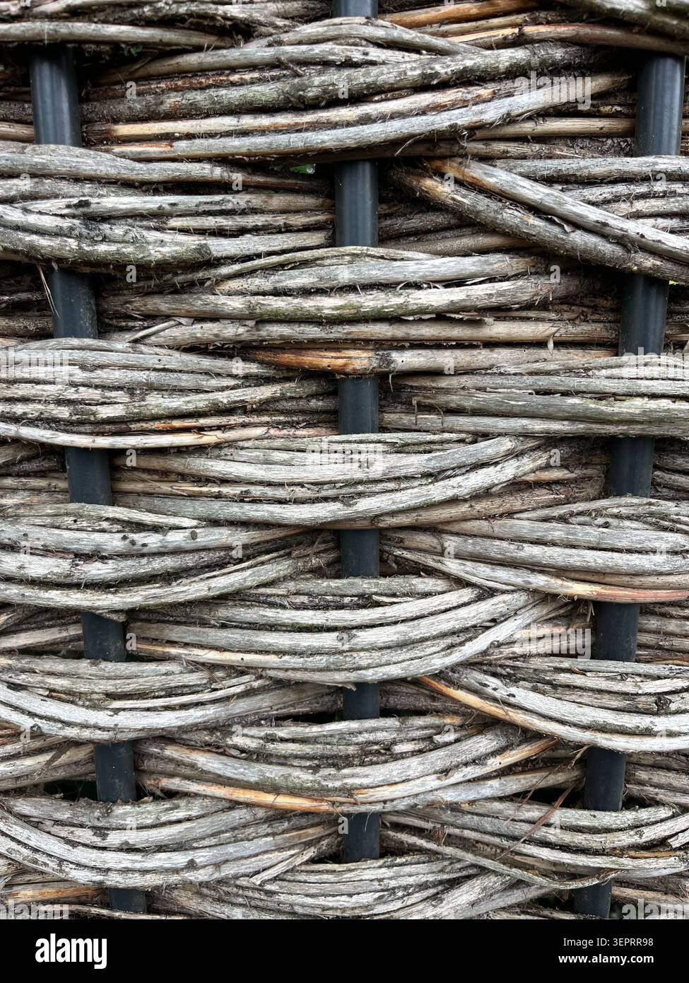 Gewebter Gartenzaun aus verwittertem Naturholzzweig mit rustikaler Textur und handgefertigten Details im Außenbereich. - Smartphone-aufgenommenes Stockfoto