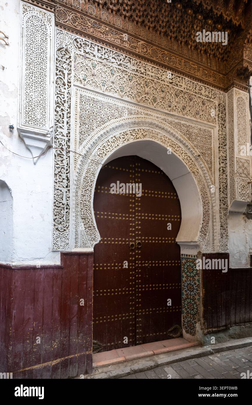 Ein kunstvoller Bogen in der Diwan-Moschee zeigt komplizierten geschnitzten Gips, geometrische Details, dunkle Holzarbeiten und traditionelle marokkanische Handwerkskunst in Fès. Stockfoto